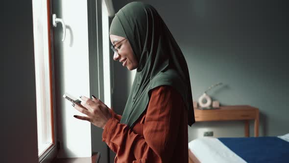 Happy Muslim woman wearing eyeglasses leafing tape by phone