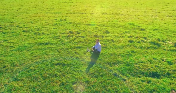 Low Orbital Flight Around Man on Green Grass with Notebook Pad at Yellow Rural Field