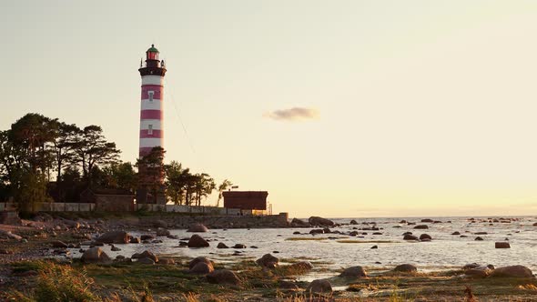 Redwhite Lighthouse on a Rocky Shore in the Warm Rays of the Sunset