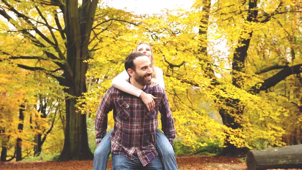 Happy couple hugging and playing piggyback ride in the wood with autumn folia