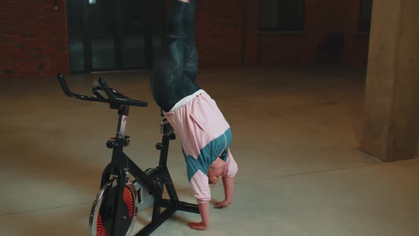 Athletic Girl Make Acrobatic Trick on Bike Exercising Workout on Stationary Cycling Machine Indoors