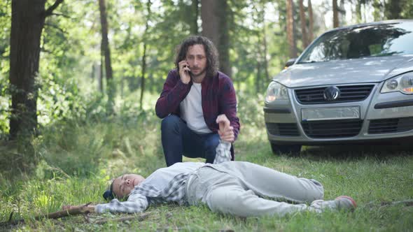 Stressed Man Calling Ambulance Checking Pulse of Knocked Down Woman Outdoors