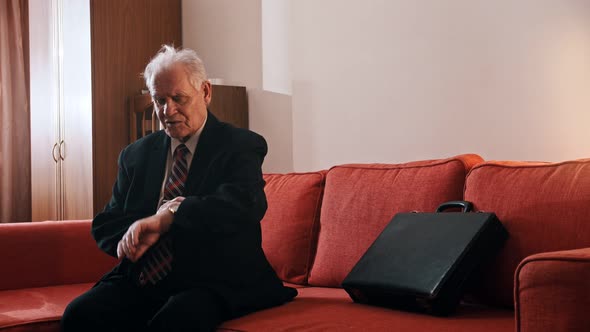 Elderly Grandfather - Grandfather Is Sitting on the Couch with a Suitcase and Checking the Time on