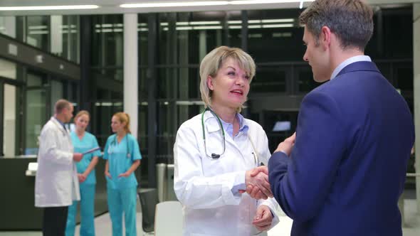 Female doctor shaking hands with businessman in corridor