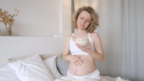 Happy Pregnant Woman Eating Cereals For Breakfast In Her Bedroom