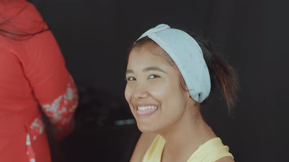 Beautiful and young woman smiling and feeling happy in cosmetics studio while make up artist prepari