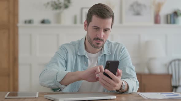 Successful Young Man Celebrating on Smartphone in Office