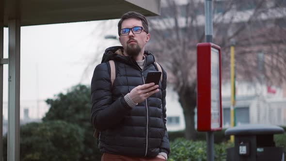 Citizen Waits for Bus at Stop Holding Smartphone