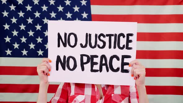 Protester Holds a Banner with a Slogan - NO JUSTICE NO PEACE - Against Background of the USA Flag