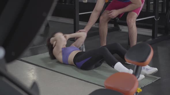 Personal Trainer Looking After Young Slim Woman Pumping Press