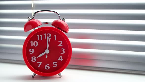Red alarm clock rang early morning eight clock morning, against background of closed blinds.