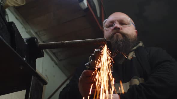 Male Repairman Cuts Metal Pipe From Which Sparks Fly with Help of an Angle Grinder Bottom View