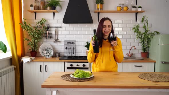 Relaxed Young Woman with Wine Glass and Bottle in Kitchen