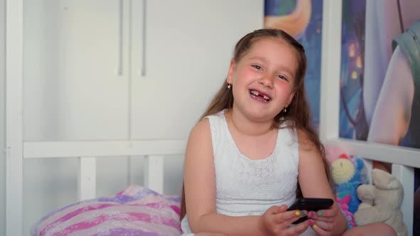 Excited little girl holding looking at smartphone at home. Attractive cute young lady female child