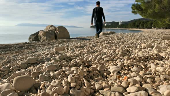 Man Walking On Pebble Beach Near Sea On Sunny Day