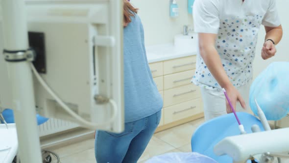 A young girl enters the office of a dental clinic and sits in the dentist chair.