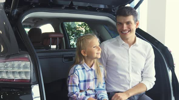 Lovely Father and Daughter Are Sitting on the Open Trunk of the Car