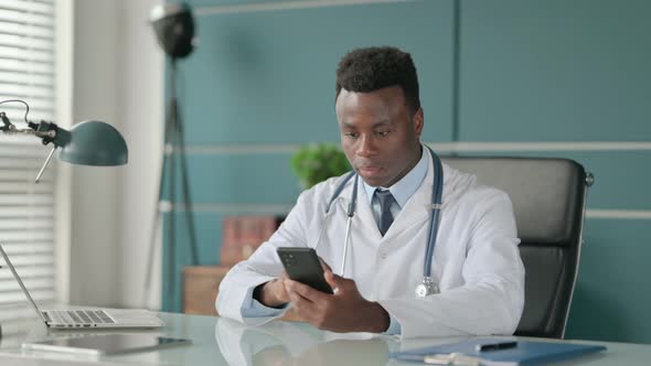 African Doctor Using Smartphone While Working on Laptop in Office