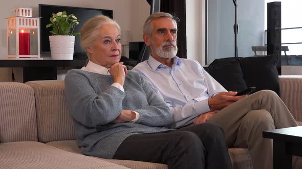 An Elderly Couple Sits in A Living Room in An Apartment and Watches Tv Serious
