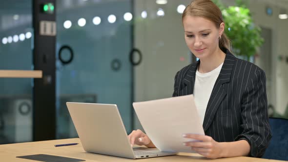 Serious Businesswoman with Laptop Reading Documents in Office 