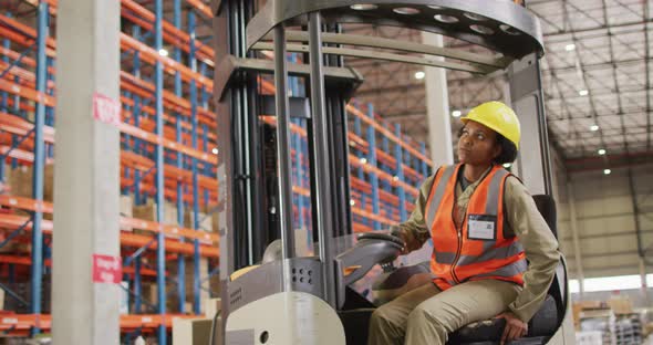African american female worker wearing safety suit and sitting in turret truck in warehouse