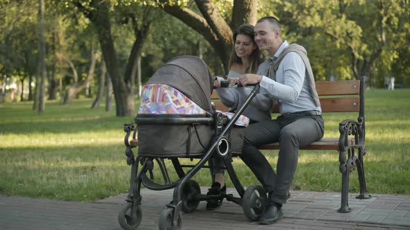 Wide Shot of Happy Loving Couple of Young Parents Sitting with Baby Carriage in Summer Park and