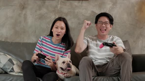Asian couple is playing video games and pet dog nearby.