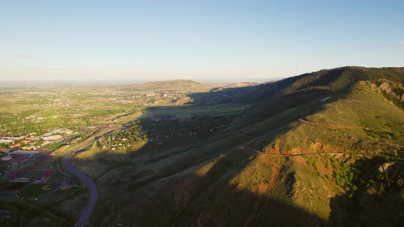 Aerial Drone Shot Of Warm Sunlight Hitting Mountain Face Near Small Town Suburbs In Golden Colorado