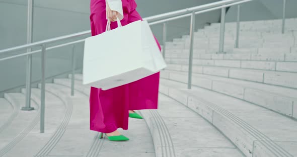 Woman in Pink Pants with White Shopping Bags Walking By Stairs in Modern City 