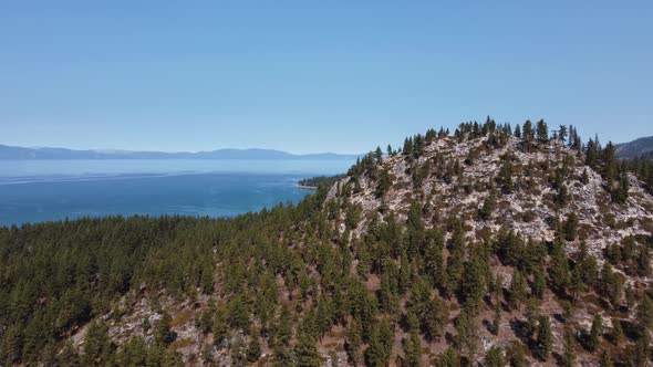 Drone shot revealing the mountains and the calm waters of Lake Tahoe from a tree-covered hill in the