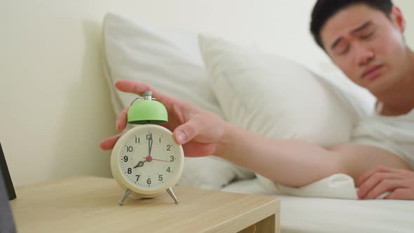 Asian attractive young man turn off alarm clock ringing in the morning.