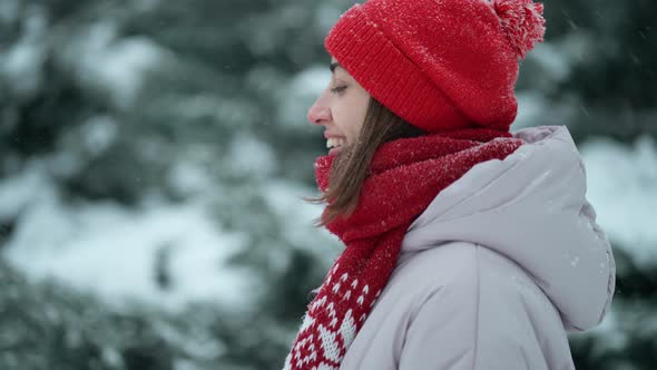 Slow Motion Beautiful Smiling Woman in Red Beanie and Scarf Standing in Forest at Snowy Winter Day