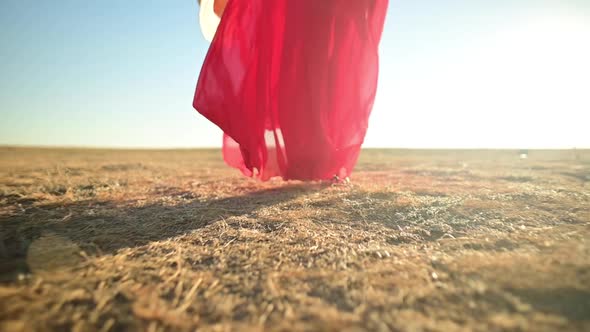 Closeup Female Slender Legs in Sandals in a Red Loose Transparent Dress That Flutters in the Wind in