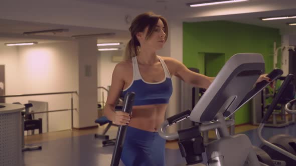 Slim Girl with Shapely Brawny Body Using Elliptical Trainers for Warm Up