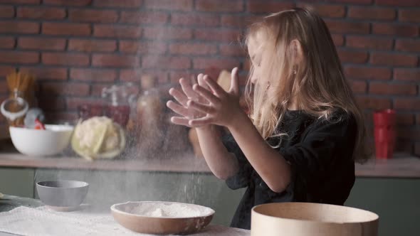 Young Girl Is Clapping Hands in Flour in a Kitchen