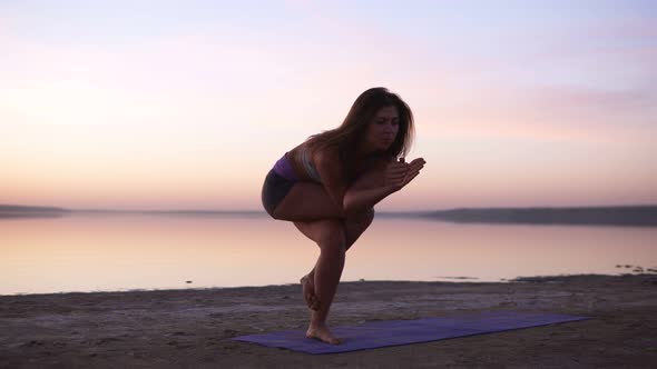 Beautiful Young Sporty Woman Wearing Sportswear Working Out in Front of the Sea or Lake Doing Eagle