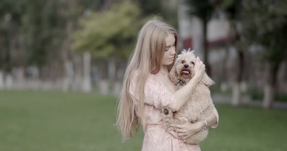 A beautiful girl, blonde, is holding a poodle dog in her hands