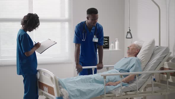 Two Black Doctors are Talking to a Patient Lying in a Hospital Room