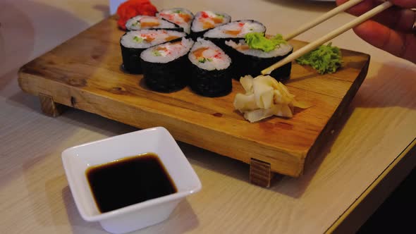 To eat rolls with chopsticks in a restaurant - a portion of sushi on a tray, ginger, wasabi, dip in