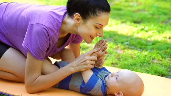 Mother playing with baby lying on mat in summer park alt