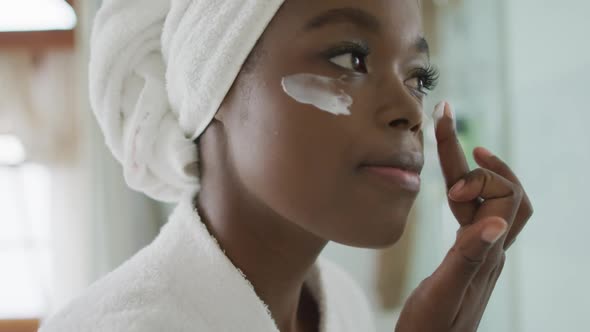 Portrait of african american attractive woman applying face cream in bathroom