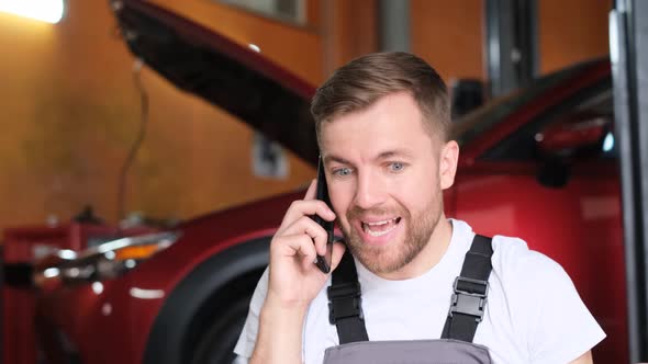 An Angry Car Mechanic is Talking on a Smartphone He is Shouting Loudly Into the Phone