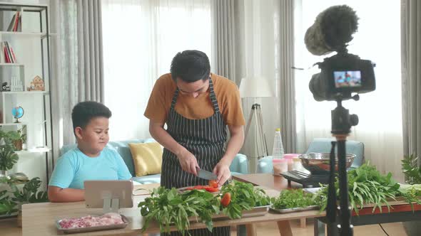 Asian Father And Son Streaming Live Video With Camera To Share Online While Cooking At Home