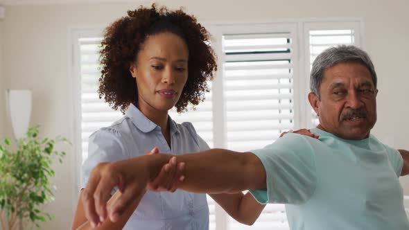 Mixed race female physiotherapist helping senior man stretching his arms