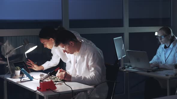 Two Mixed Race Engineers Checking Motherboard with Multimeter Tester