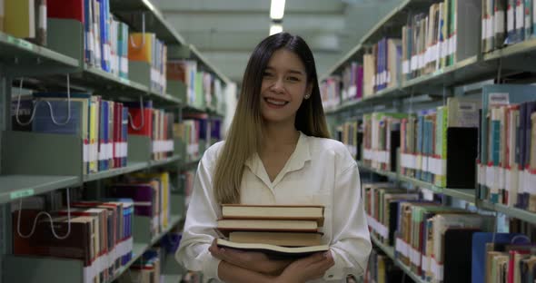 Slow motion Asian student girl with books smiling and walking in library.