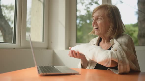 Senior Elderly Woman Having Video Chat Conference with Laptop Computer with Injury Broken Arm in