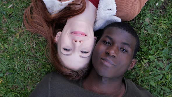 romantic mixed couple opening closed eyes and smiling at camera lying on lawn