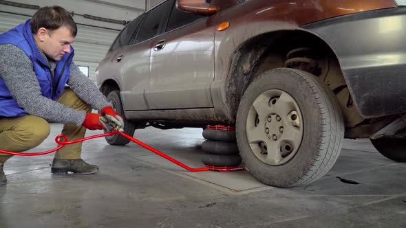 Worker raises car by pneumatic jack