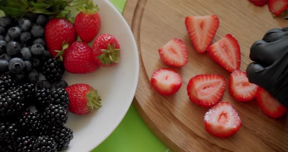 Chef in Black Gloves Slicing Fresh Strawberry on Wooden Cutting Board. Close Up Top View